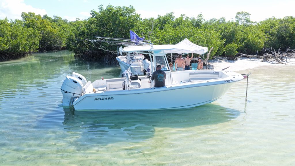 Center console boat anchored in clear shallows off a mangrove-lined beach
